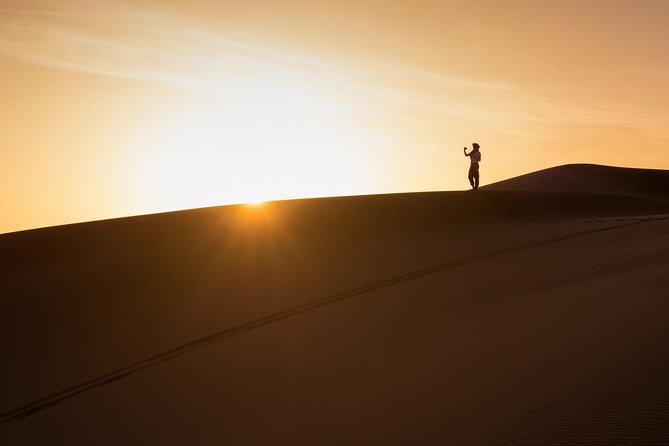 A lone figure on the crest of a Sahara dune at sunset